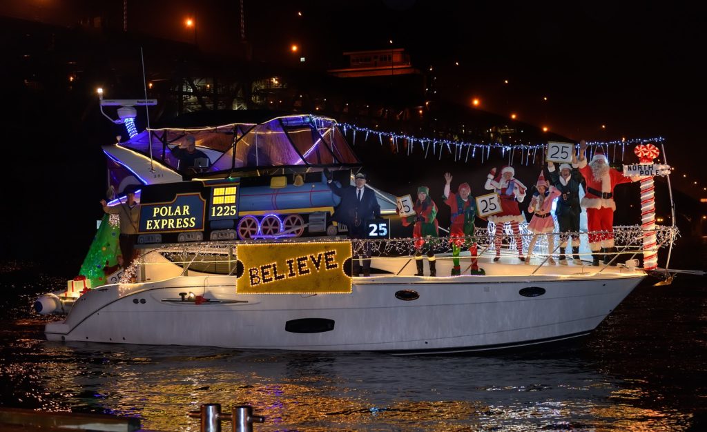Parade boat saying "Polar Express" and "Believe" with people dressed as Santa and his helpers on deck