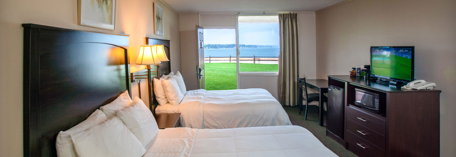 A spacious Yorktown hotel room with colonial green carpet, two queen beds, a desk, and waterfront views.