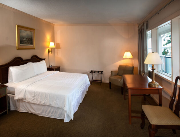 A spacious Yorktown hotel room with colonial green carpet, a king bed with white linens, a desk, and accent lighting.