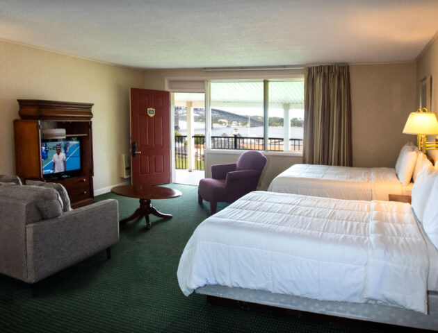 A spacious Yorktown hotel room with colonial green carpet, two full beds, a sofa set, and a TV.